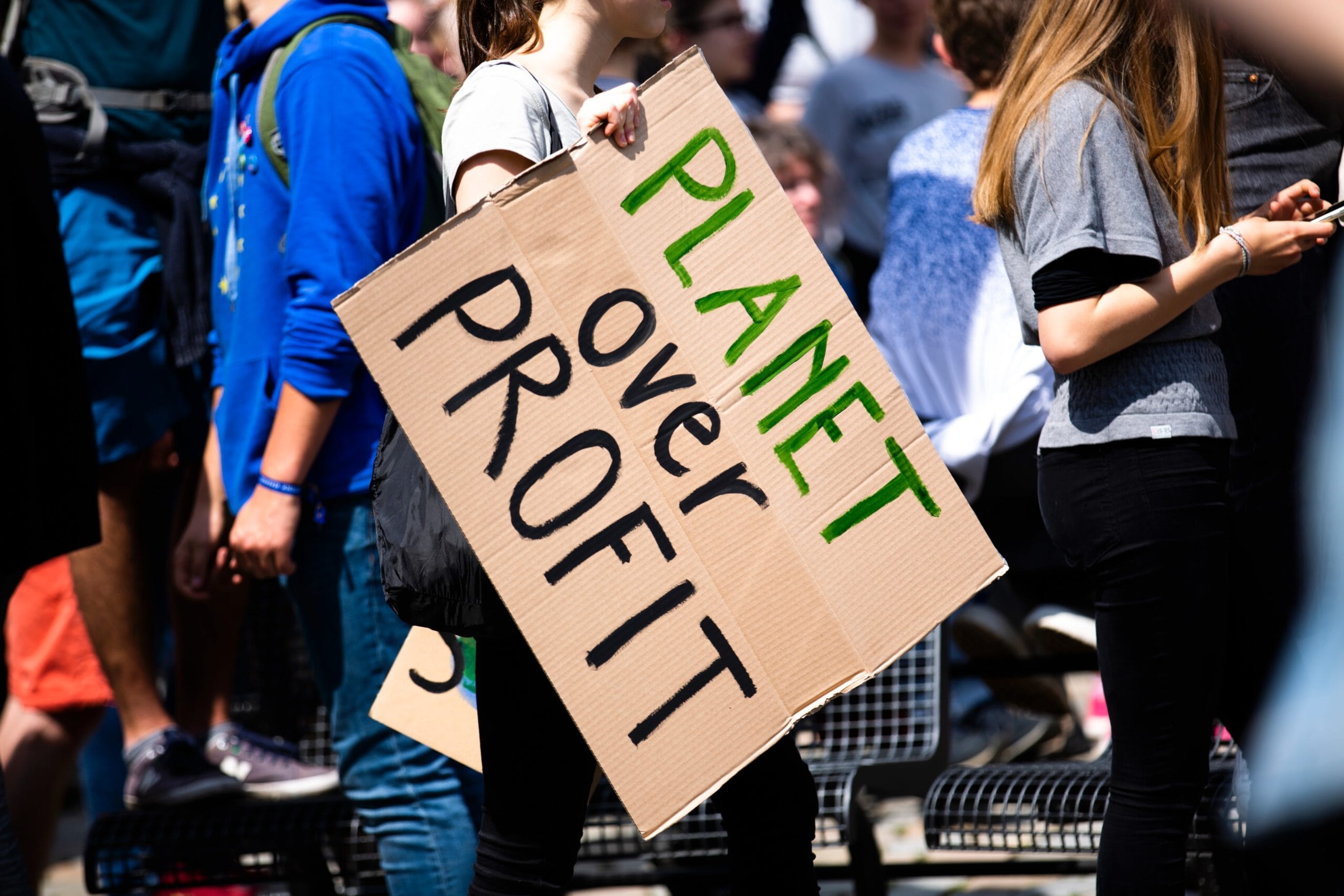 Image of woman at a climate protest carrying a sign that says "Planet over Profit"